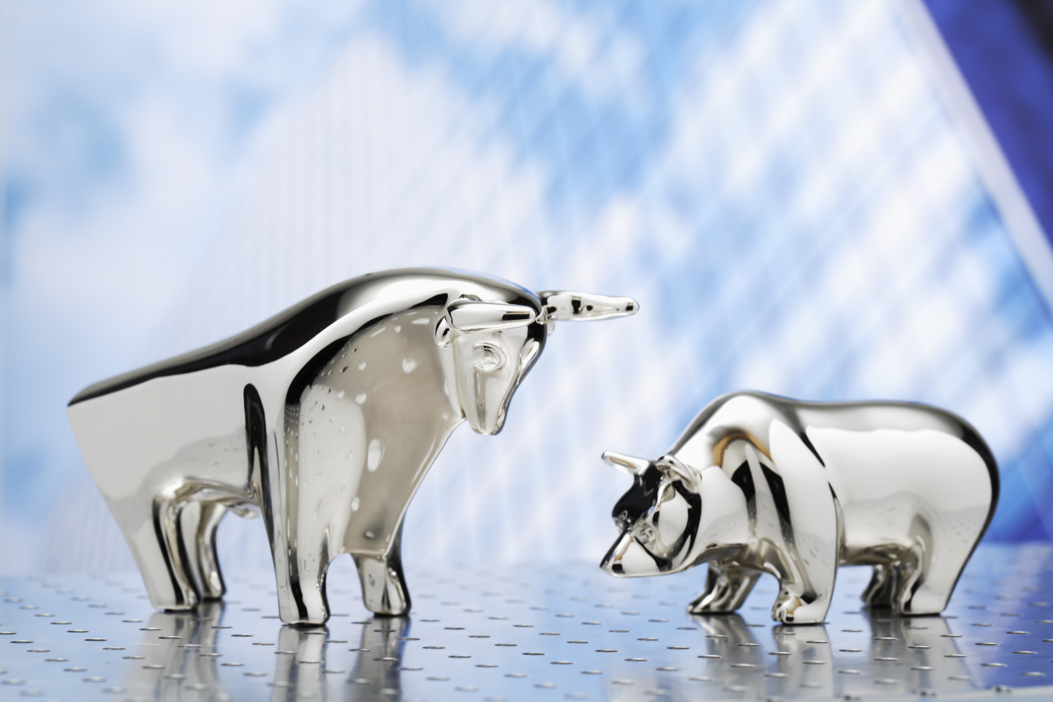 Silver bear and bull figurines against a blue background.