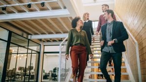 A group of four coworkers walking down the stairs in their office building.