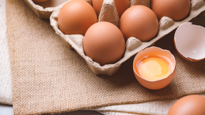 A carton of eggs is placed on top a burlap bag. One egg is cracked open. Why is the cost of eggs rising?