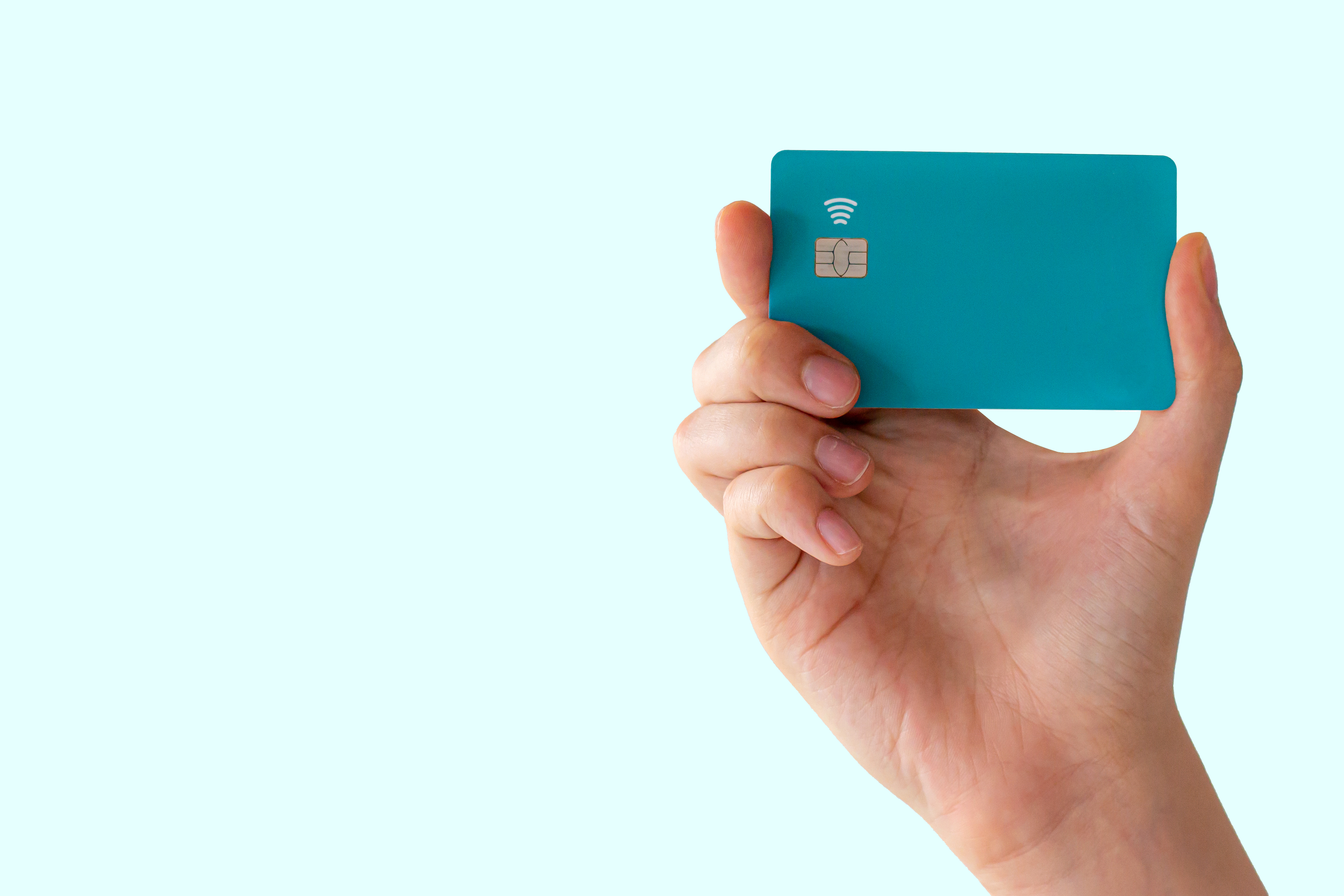 A hand holding a credit card with a plain, blue background.