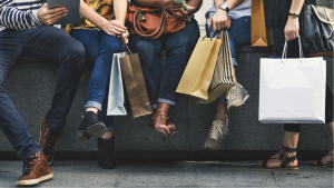 Friends sit on a ledge with shopping bags after shopping retail stores. Retail Stocks to Buy