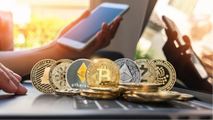 hot cryptos to buy: Various cryptocurrency coins are on a computer in front of someone holding a phone. cryptos for huge profits. cryptos to buy