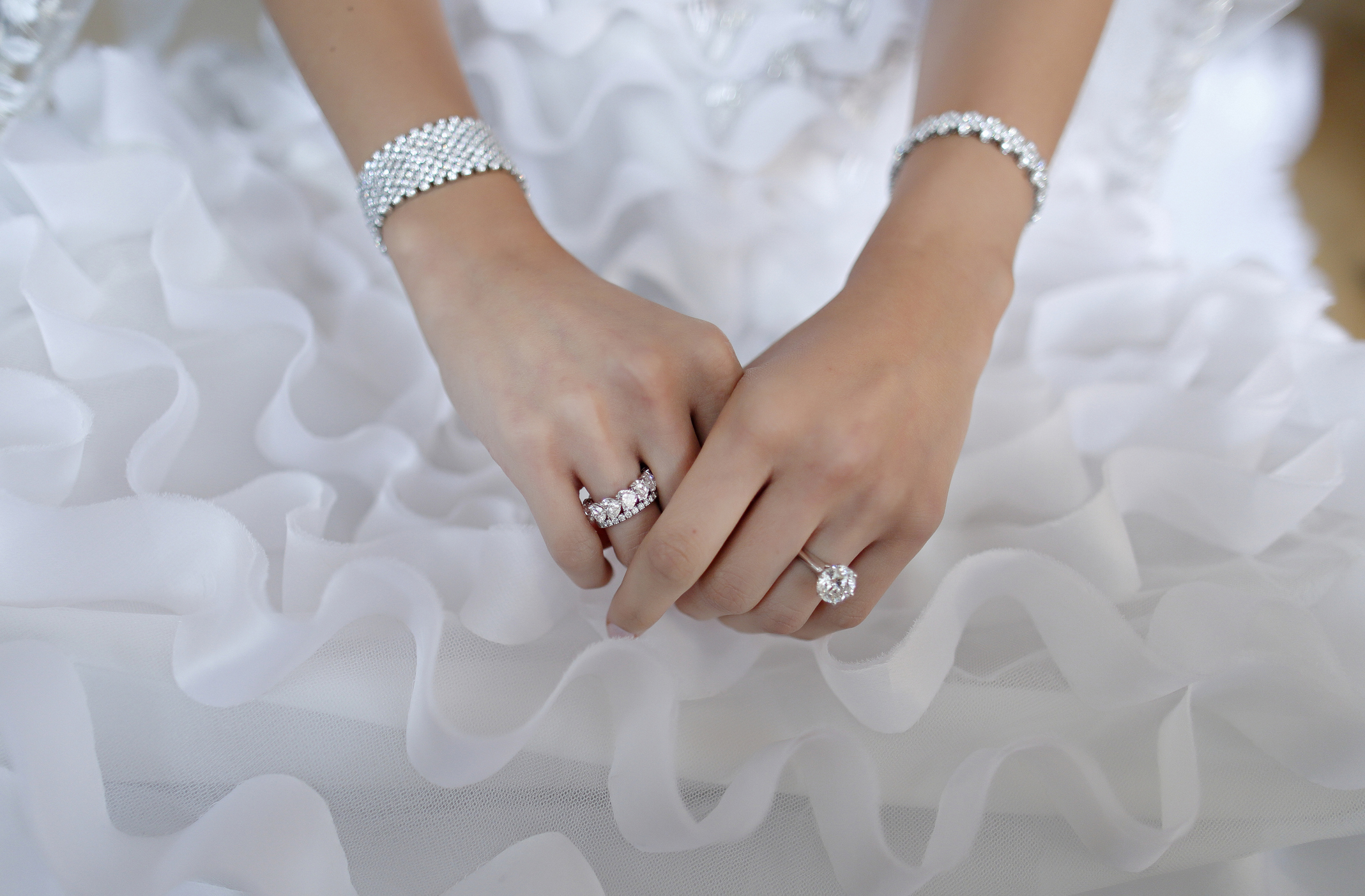 Two hands with jewelry over a wedding dress.