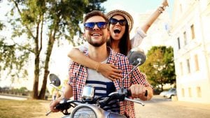 A photo of an excited woman riding on the back of a bike a man is driving.