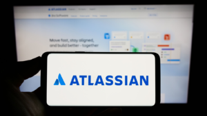 Person holding cellphone with logo of Australian software company Atlassian Corporation (TEAM) on screen in front of webpage. Focus on phone display. Unmodified photo.