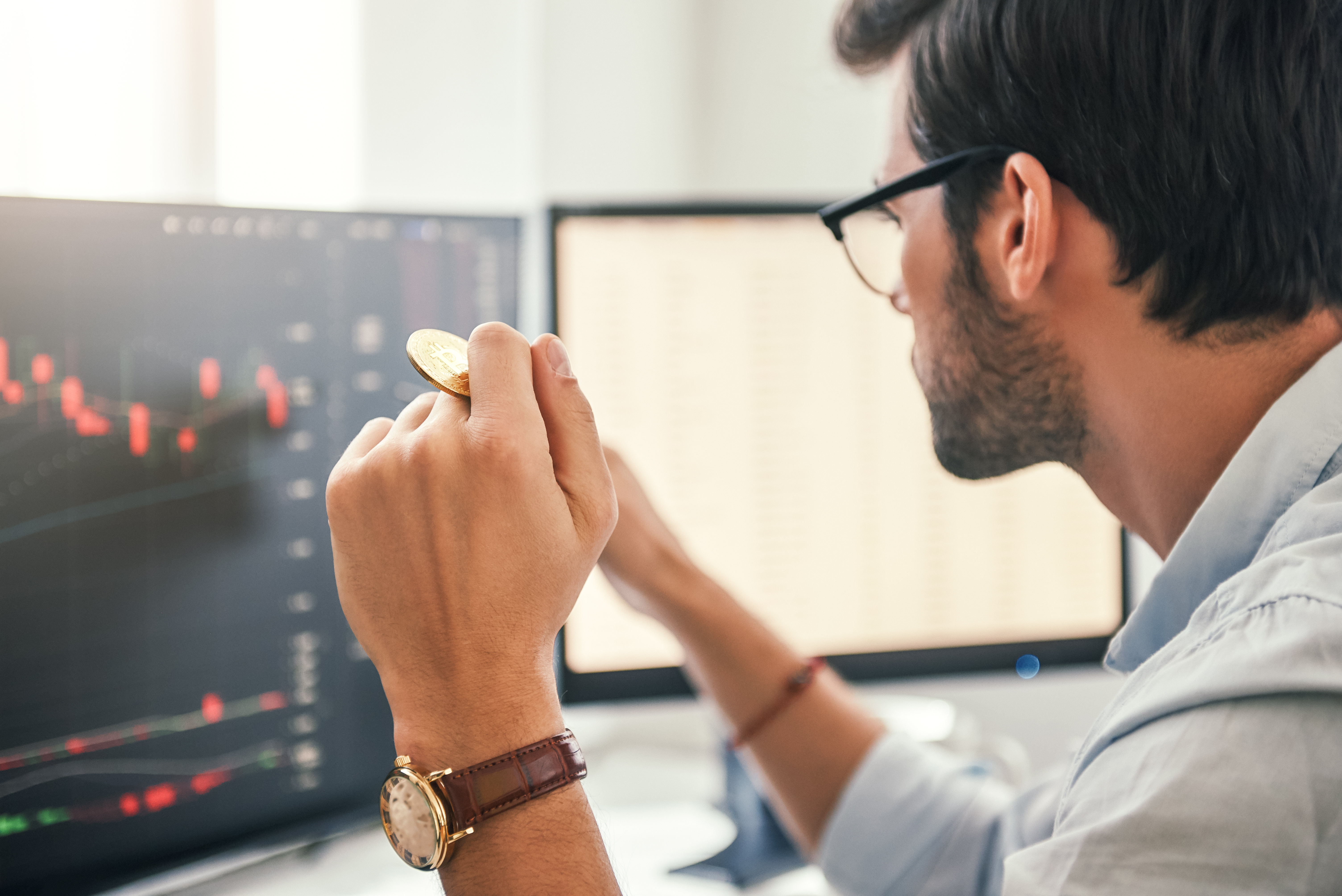 Investor looking at chart on screen holding gold coin