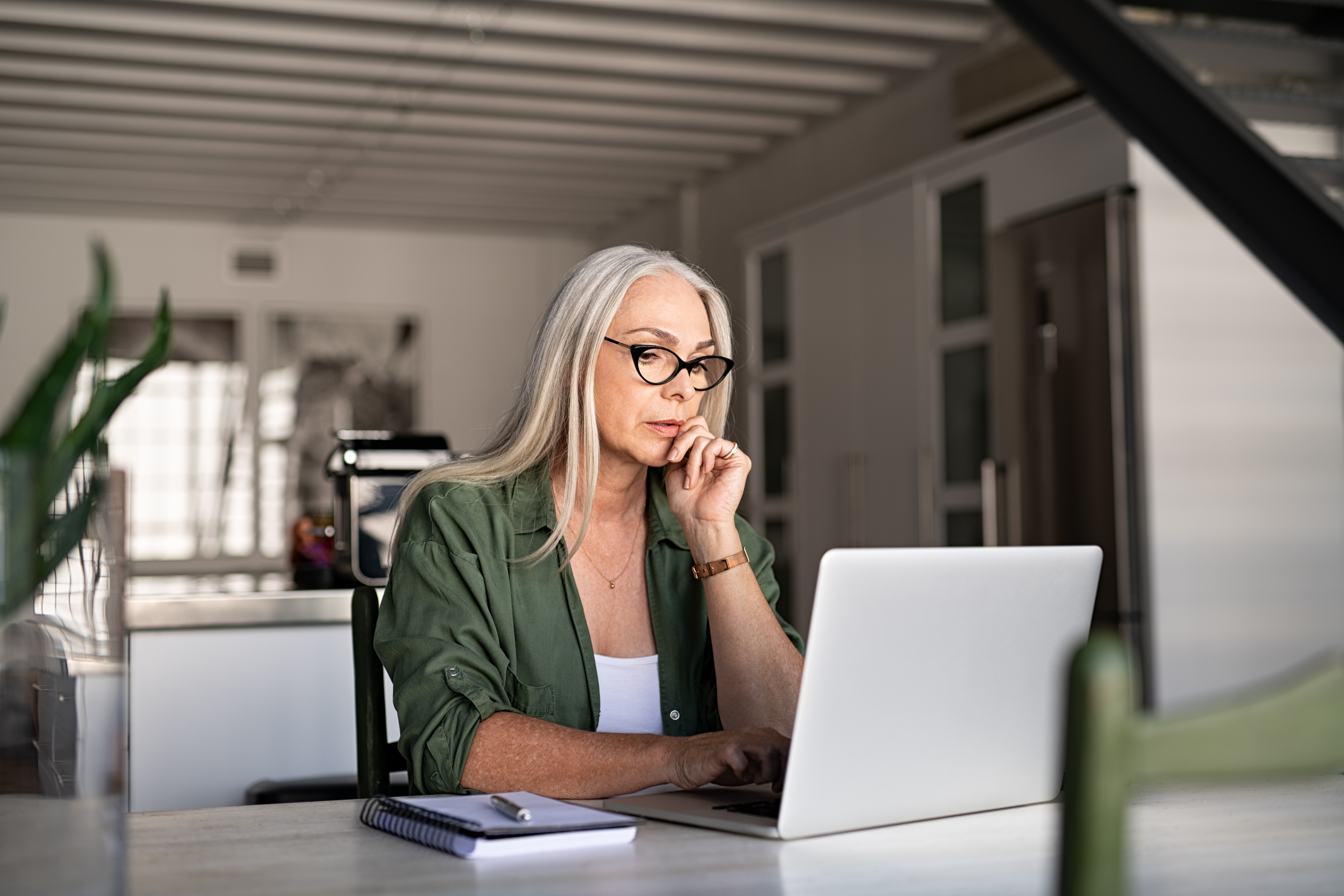 Person with hand on chin typing on laptop.