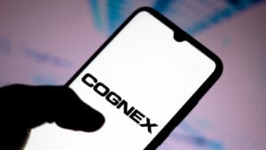 Cognex (CGNX) logo displayed on smartphone with pink and blue background behind, symbolizing CGNX stock