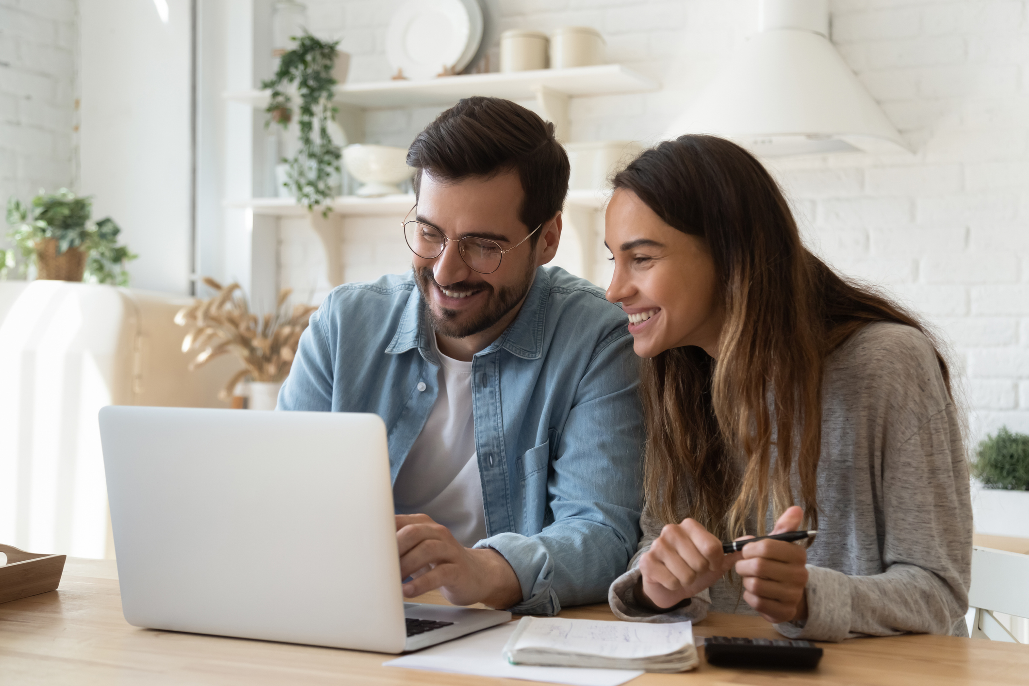 Two investors in a living room smile while looking at something on a laptop.