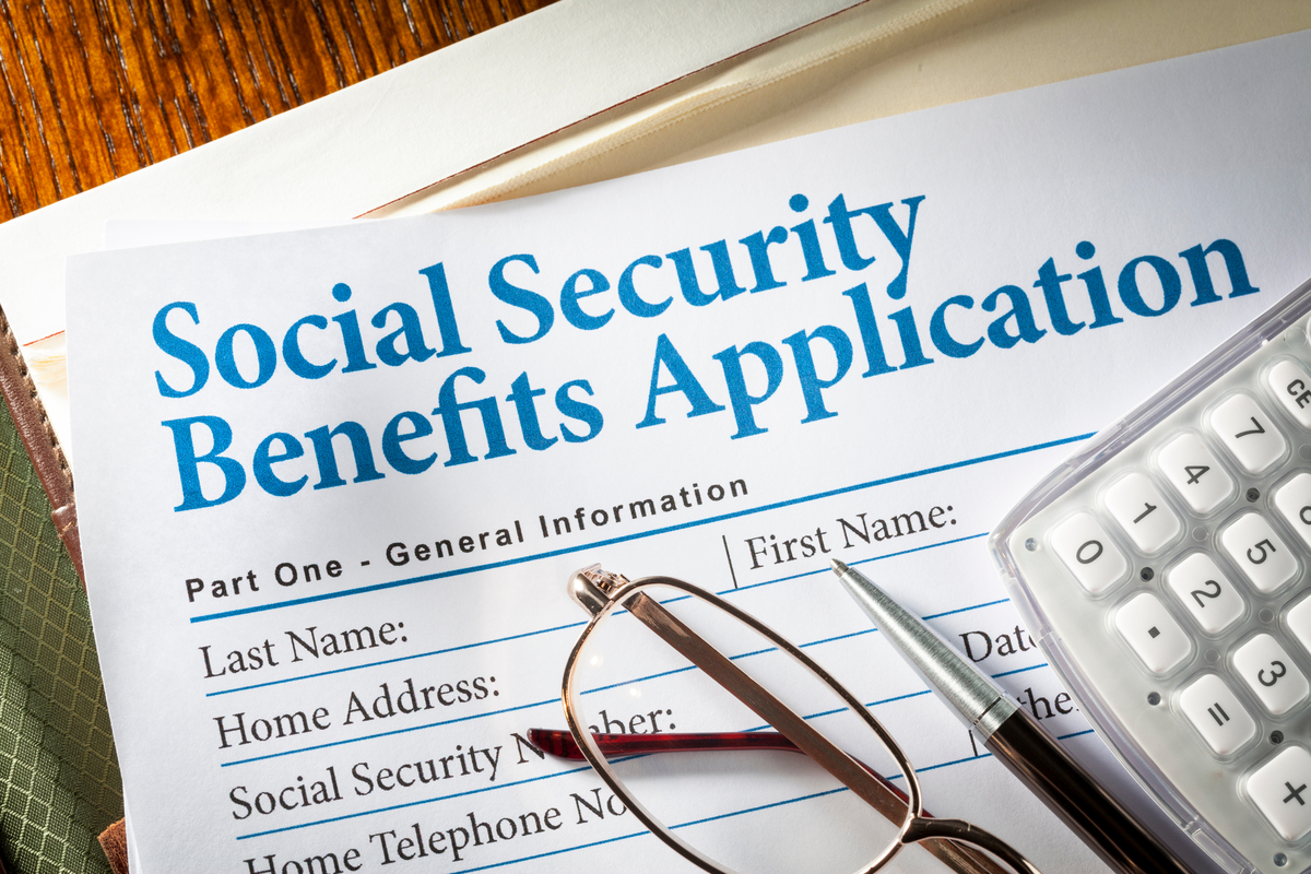 Glasses, pen, and calculator on form labeled Social Security Benefits Application.