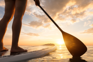 Stand up paddle boarding on a quiet sea with warm summer sunset colors, close-up of legs