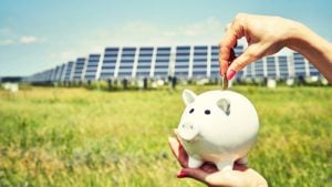 Solar penny stocks: Piggy bank in front of solar panel infrastructure