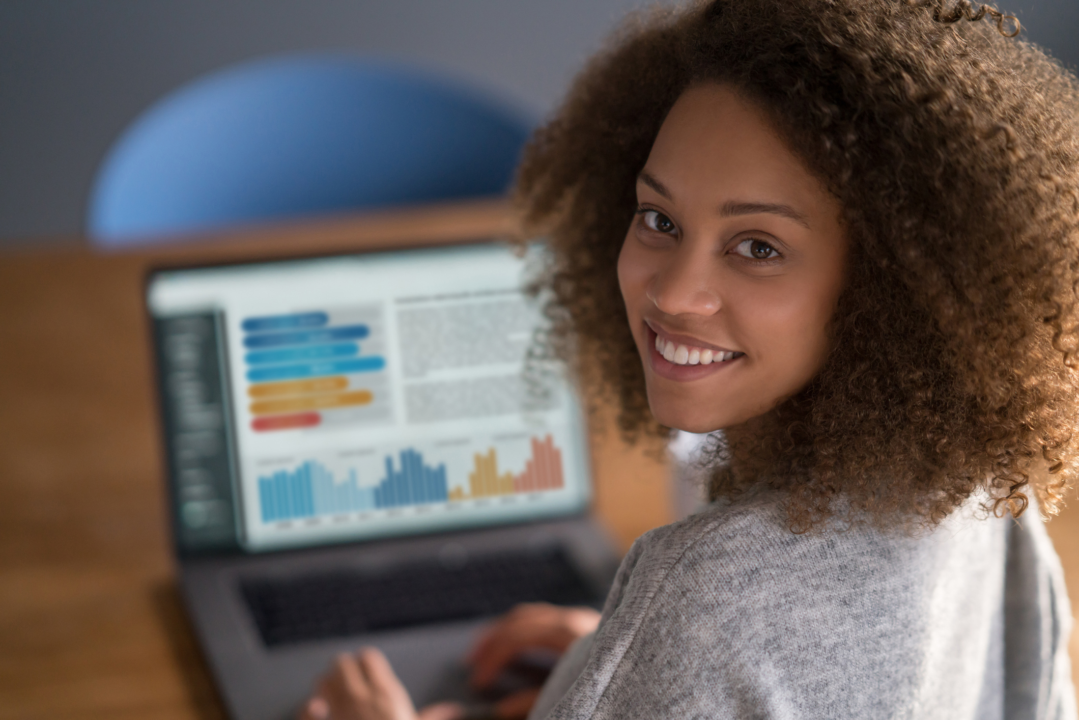 A person smiling while charts show up on their laptop screen. 