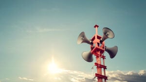 Photo of alarm tower with speakers against blue sky, representing warning