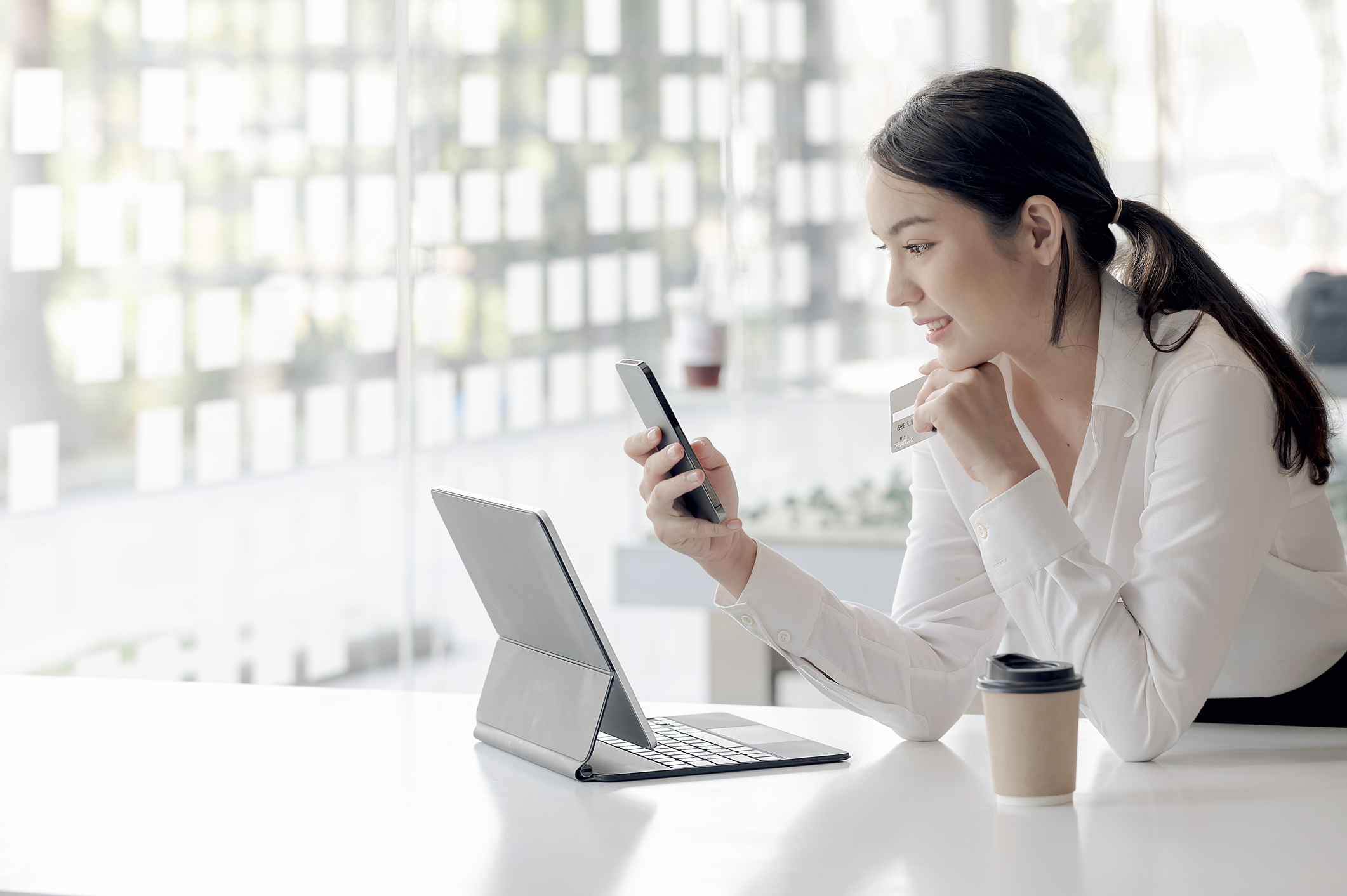 A person uses a smartphone and a laptop in a coffee shop.