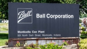 An image of a black sign surrounded by flowers and trees that has the white text "Ball" with an underline in a white box, the text "Ball Corporation" in white, and the text "Monticello Can Plant" 501 North Sixth Street, Monticello, Indiana below in a small white font.