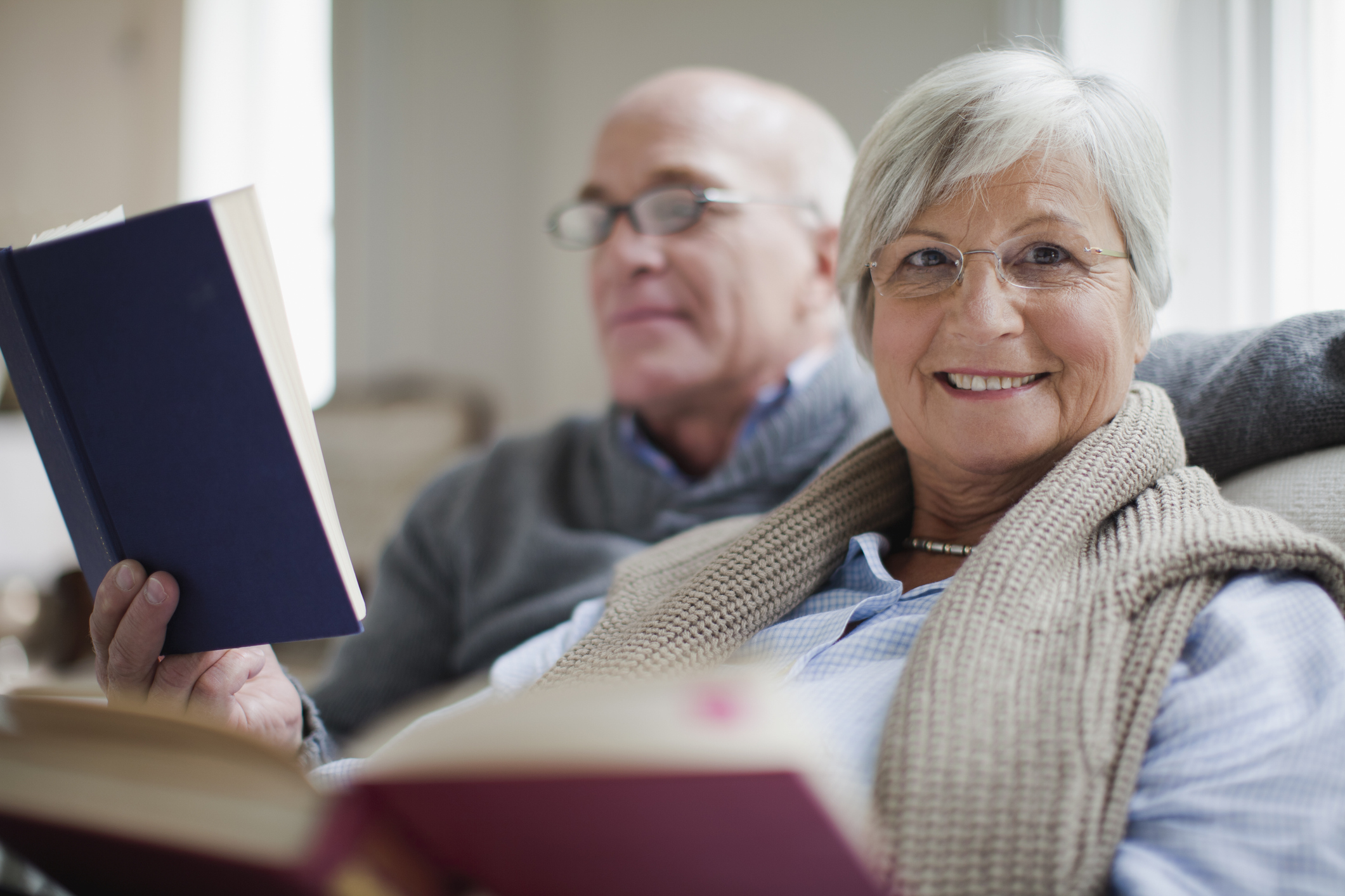 A couple is seated and reading books. One is smiling. 