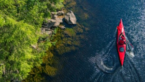 top down photo of a man in a red kayak on a pristine water way with greenery to the left