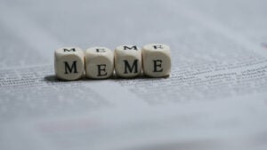 Four dice on a newspaper with letters instead of dots, spelling out the word "Meme". Meme Stocks to Sell. Meme stocks to avoid