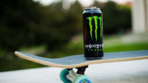 A can of Monster Beverage (MNST) energy drinks sits on top of a skateboard.