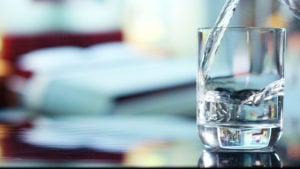 A photo of water being poured into a glass that's sitting on a table.