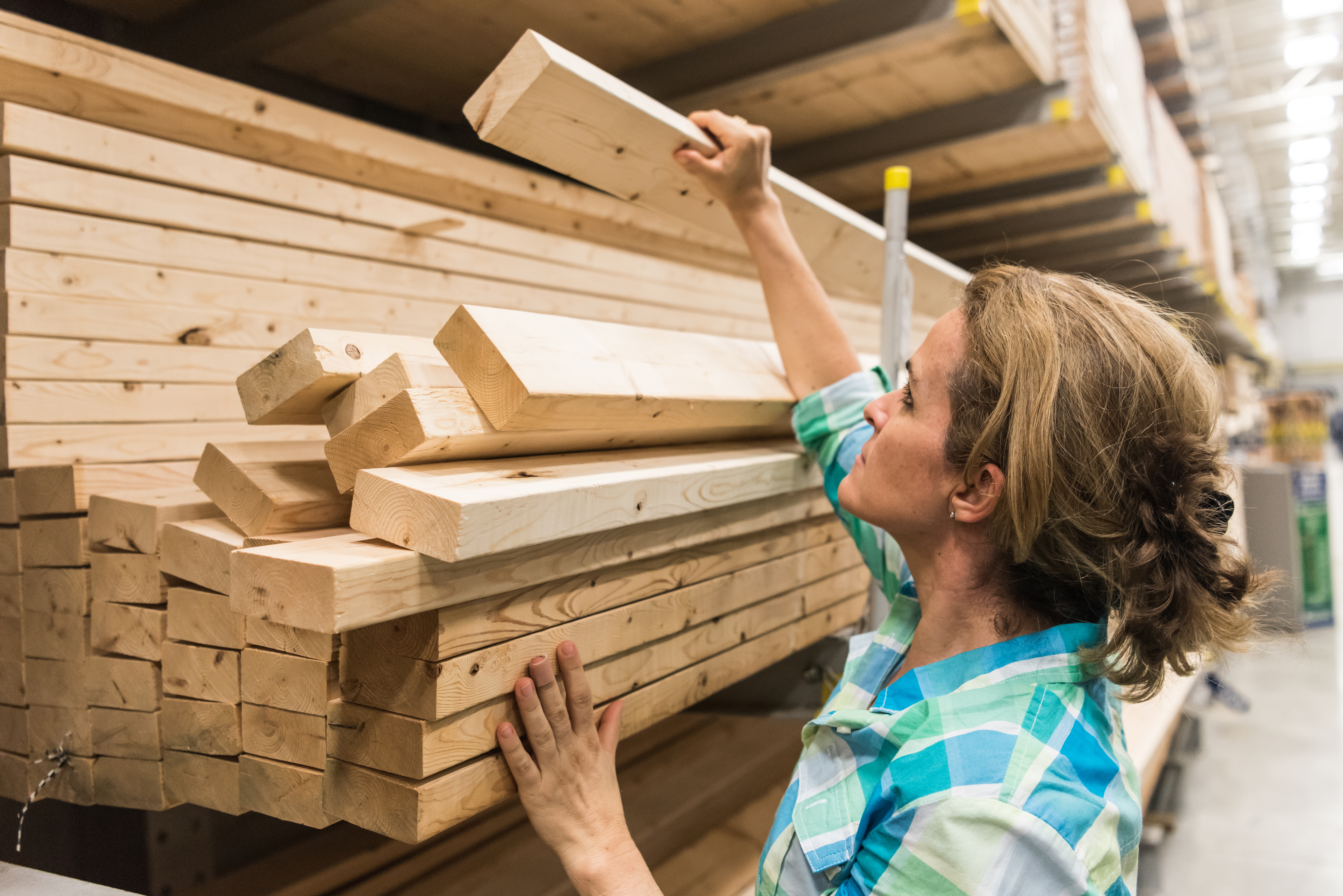 A woman taking a piece of lumber off a stack in a store.