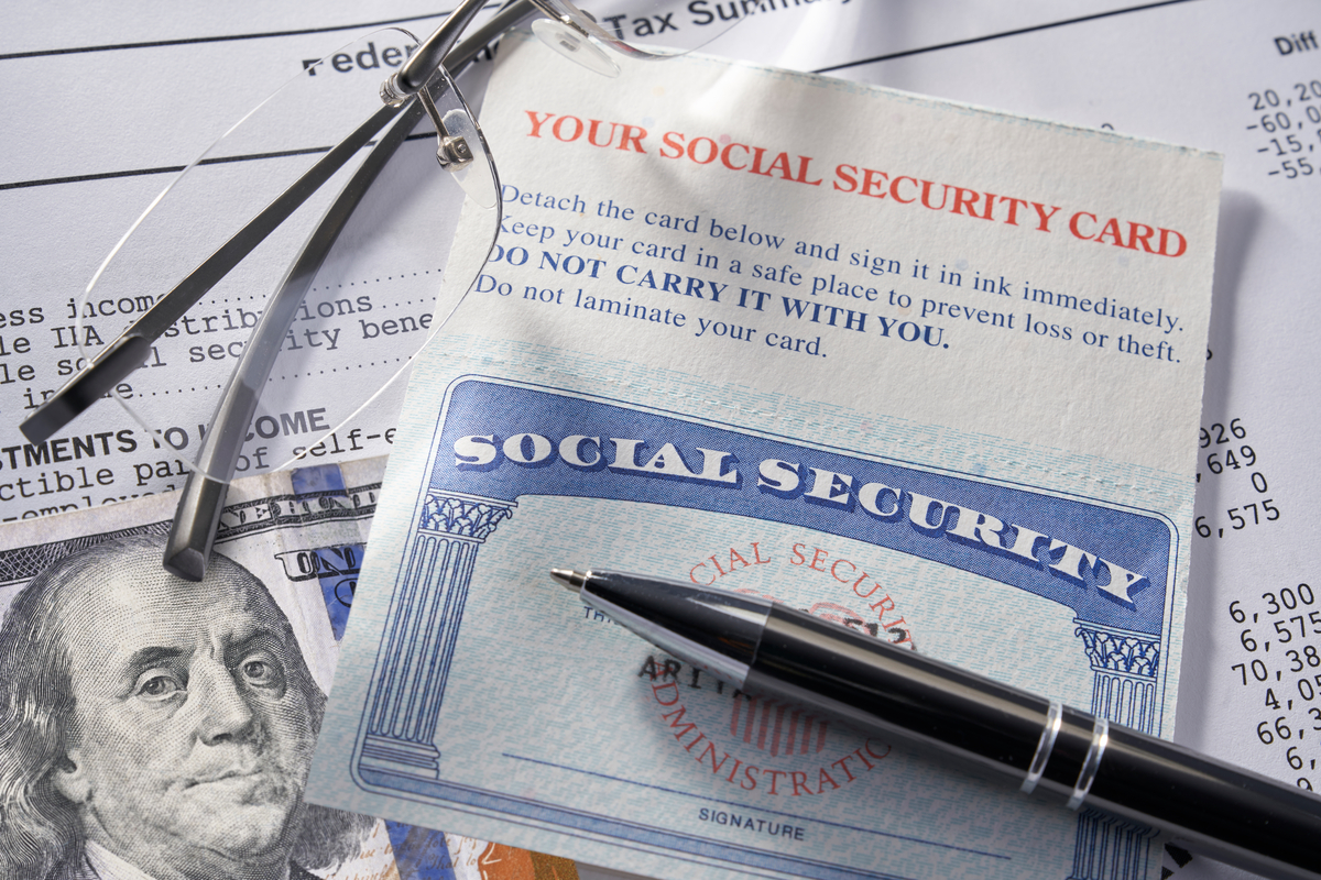 A Social Security card with a pen, $100 bill, glasses, and a piece of paper.