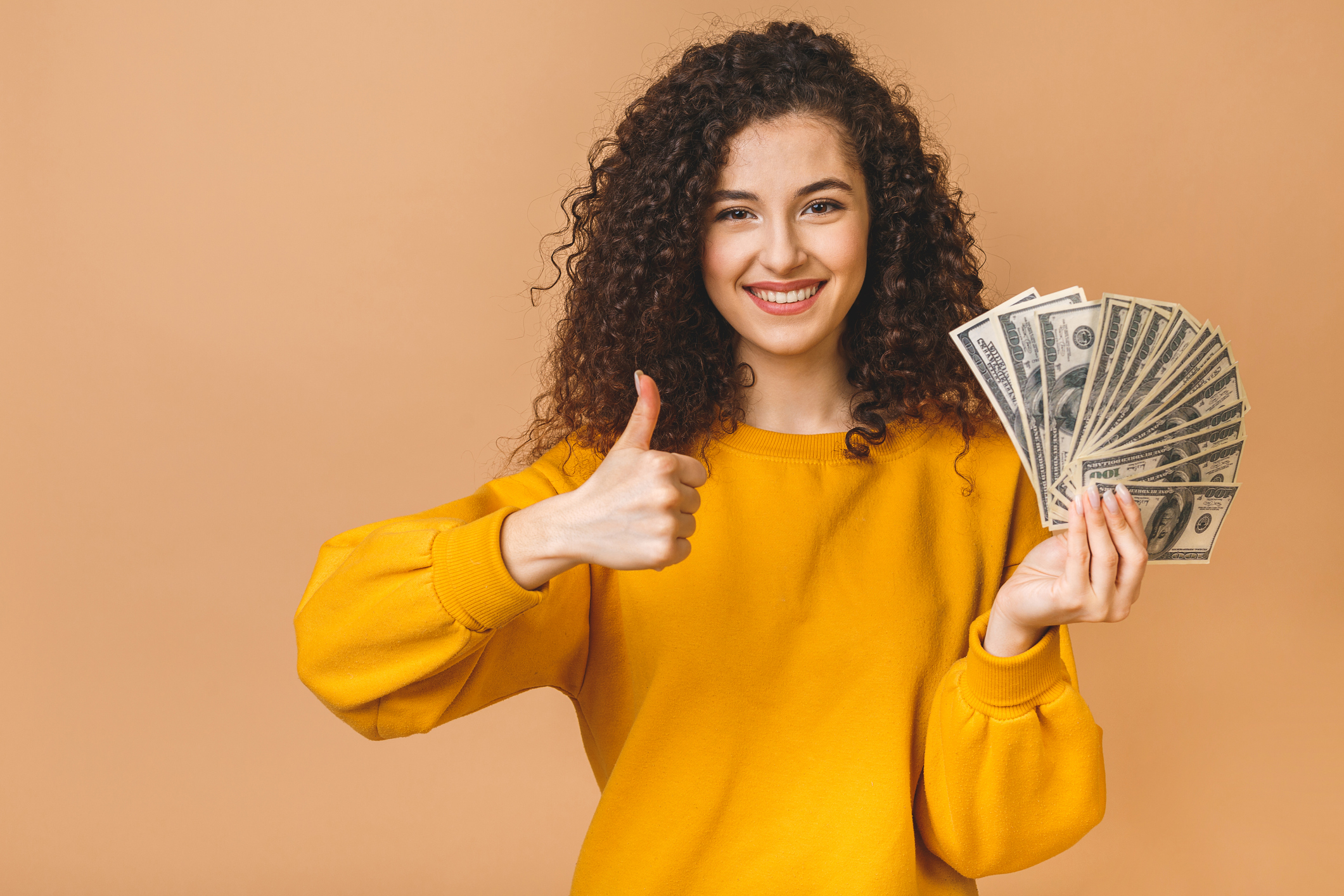 A person holding a fan of money and holding up a thumbs up sign.