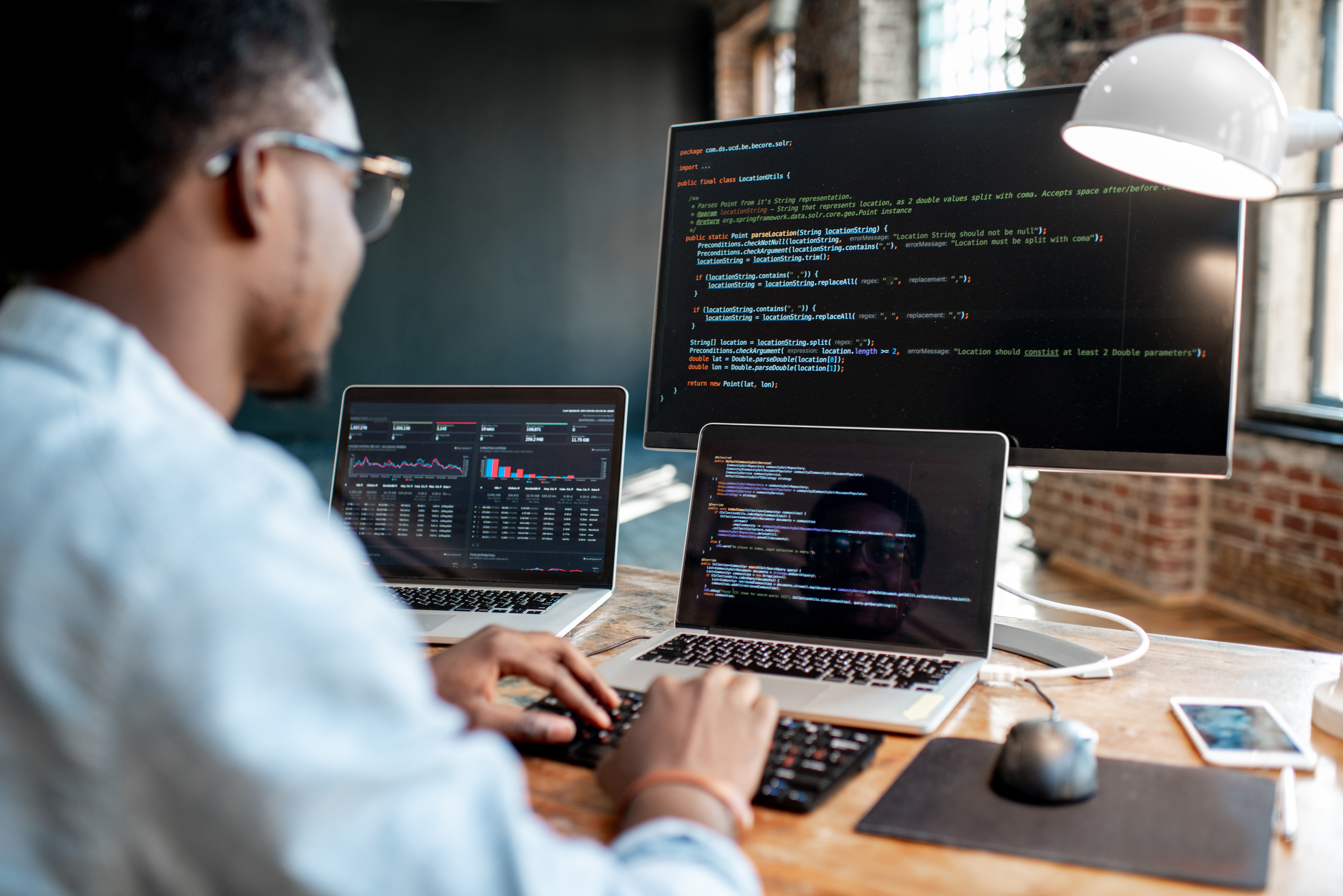 A man looking at code on multiple computer screens.