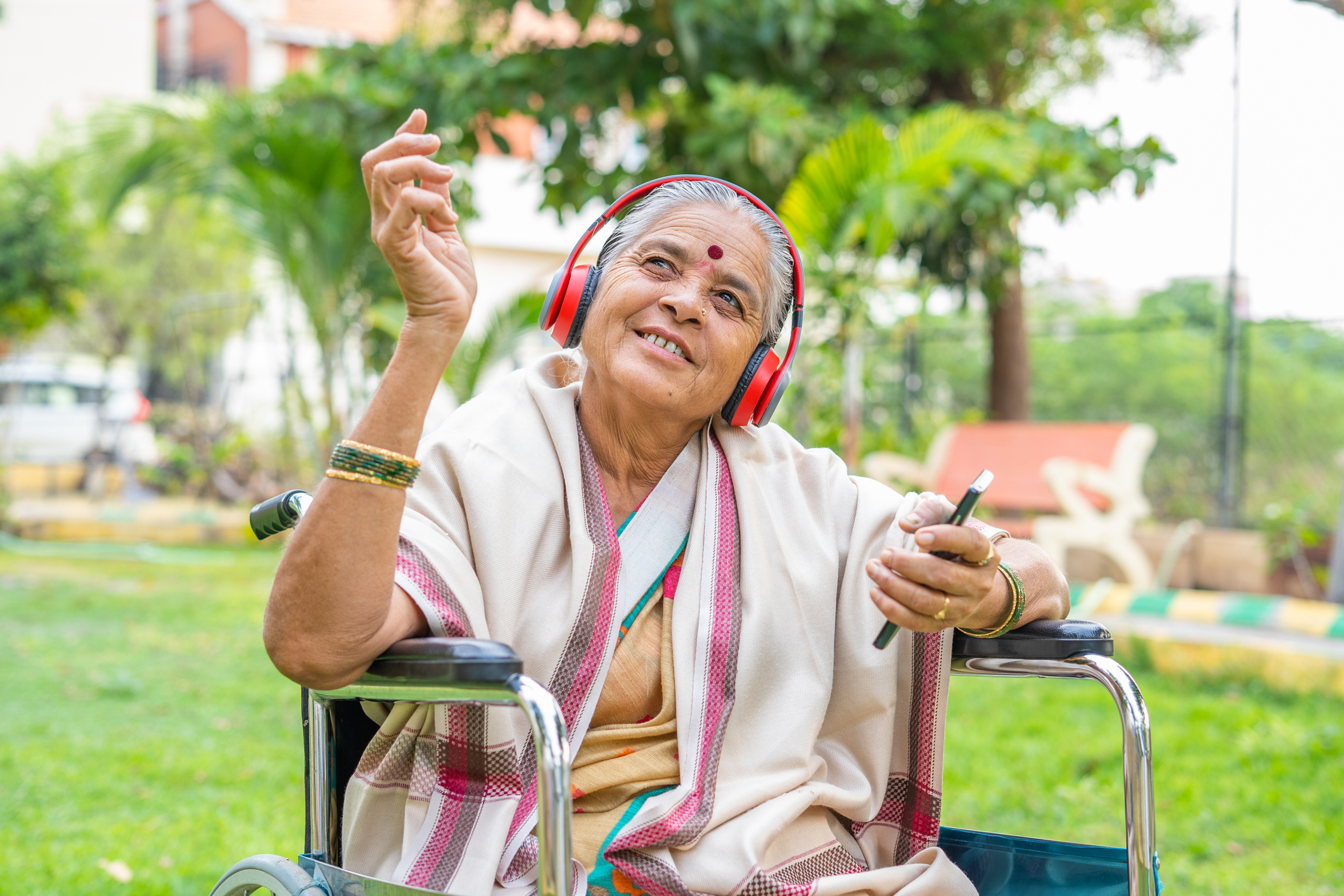 Someone is seated outdoors, smiling, looking up, and holding a phone.