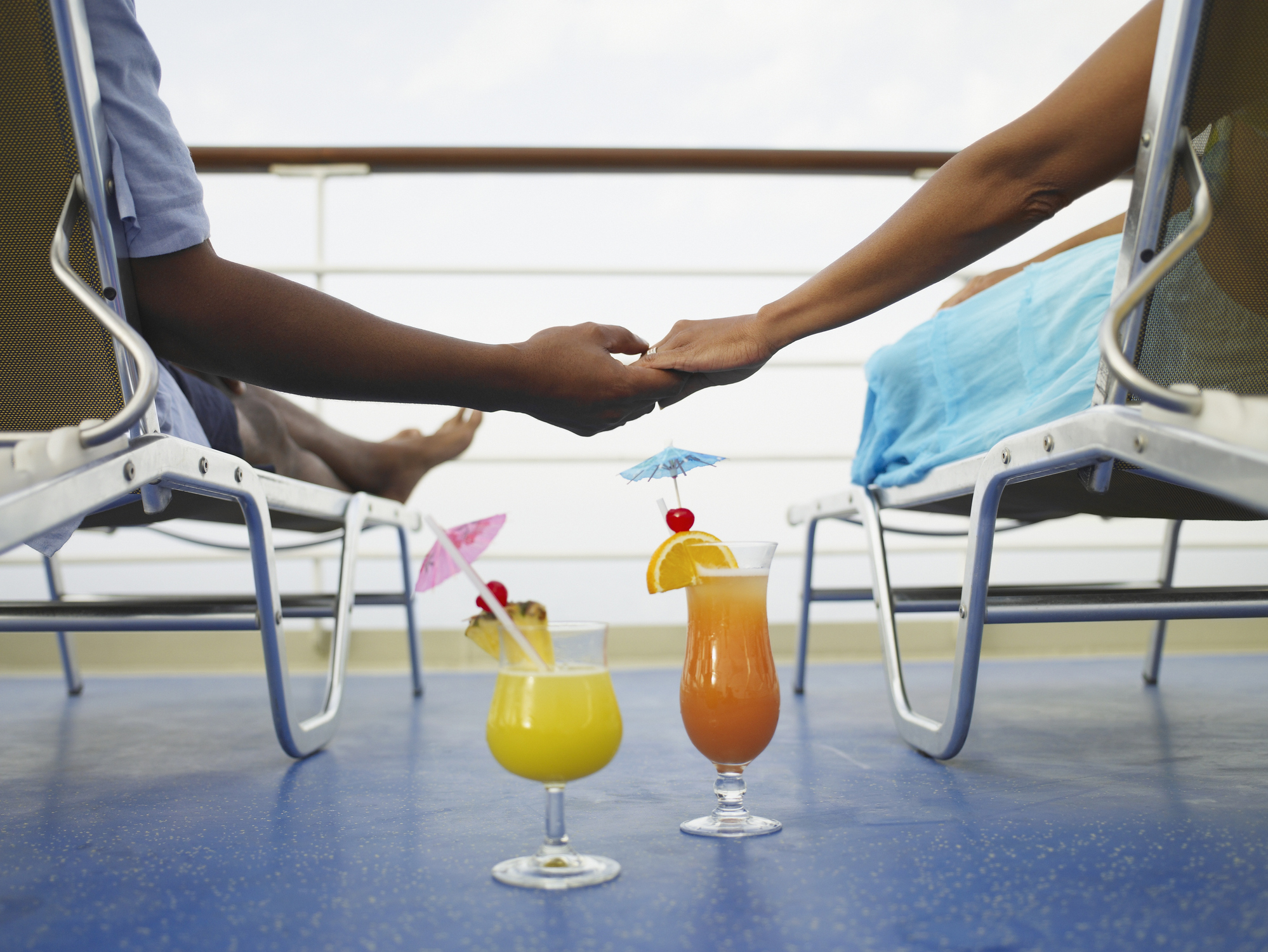 Two people holding hands on a cruise ship with tropical drinks between them.