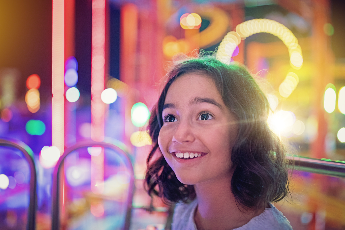 A child smiles with bright amusement park lights in the background. 