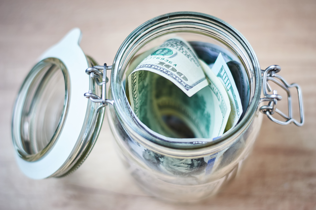 A jar full of $100 bills on a table.