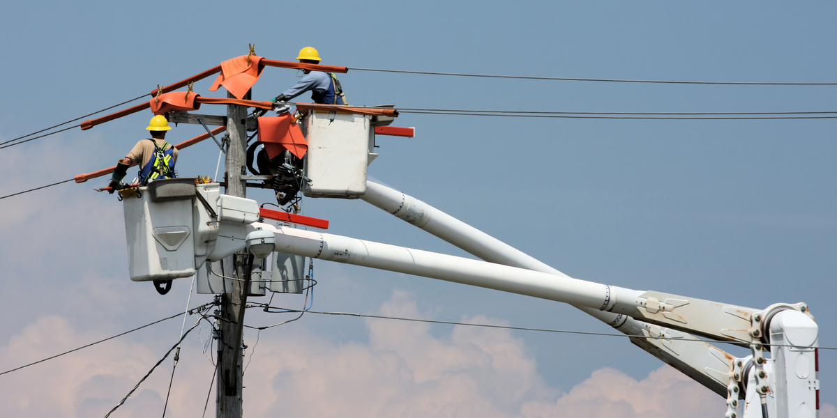 Two people wearing personal protective equipment and working on power lines. 