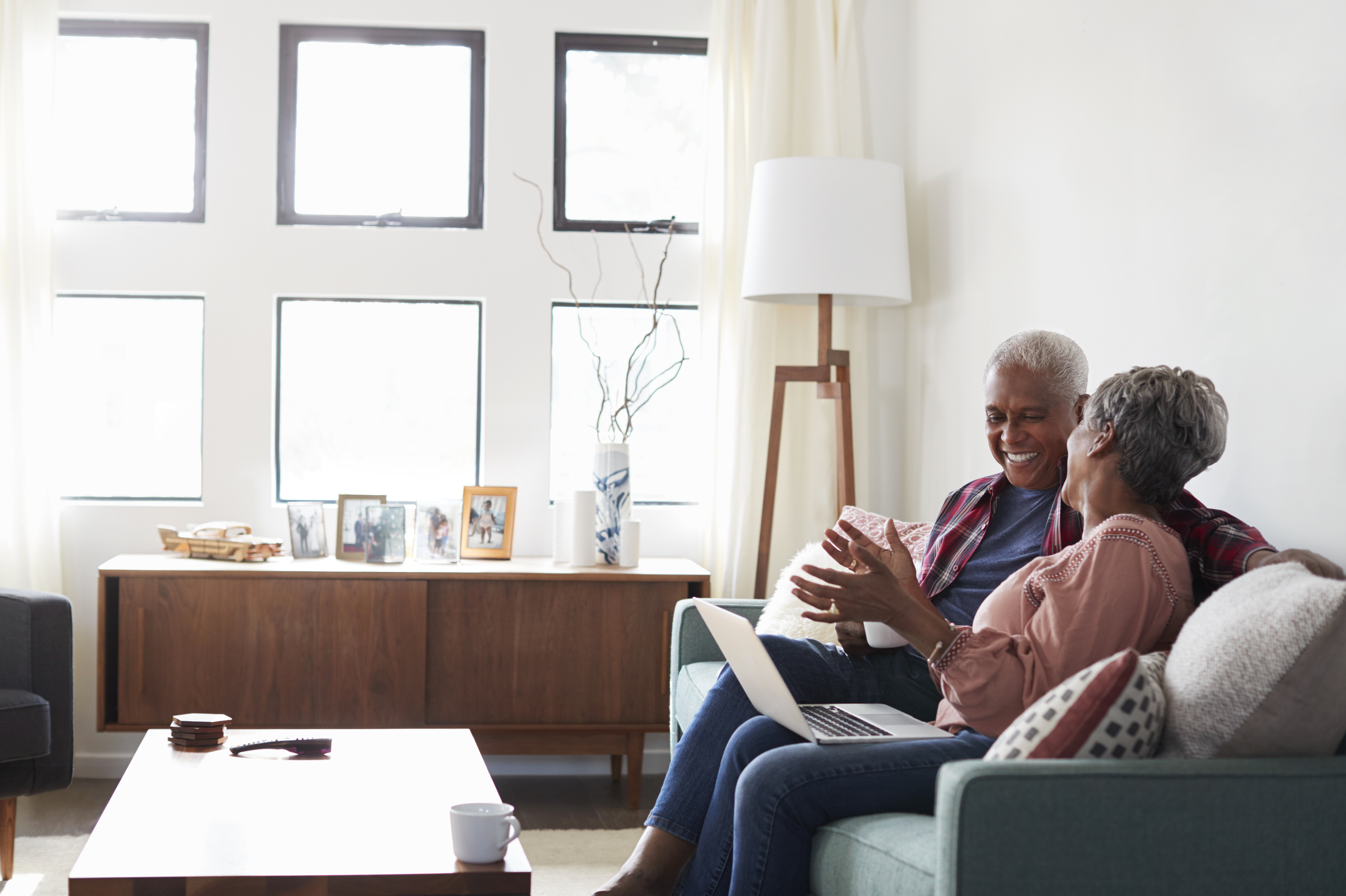 Two people sitting on a couch smiling and looking at a laptop.