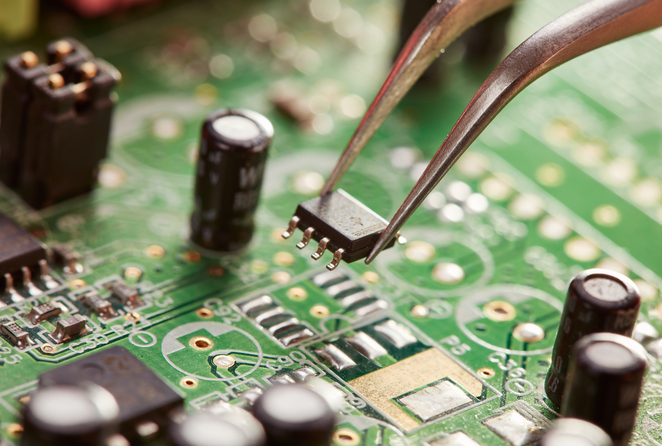 A pair of tweezers holding a chip above a circuit board.