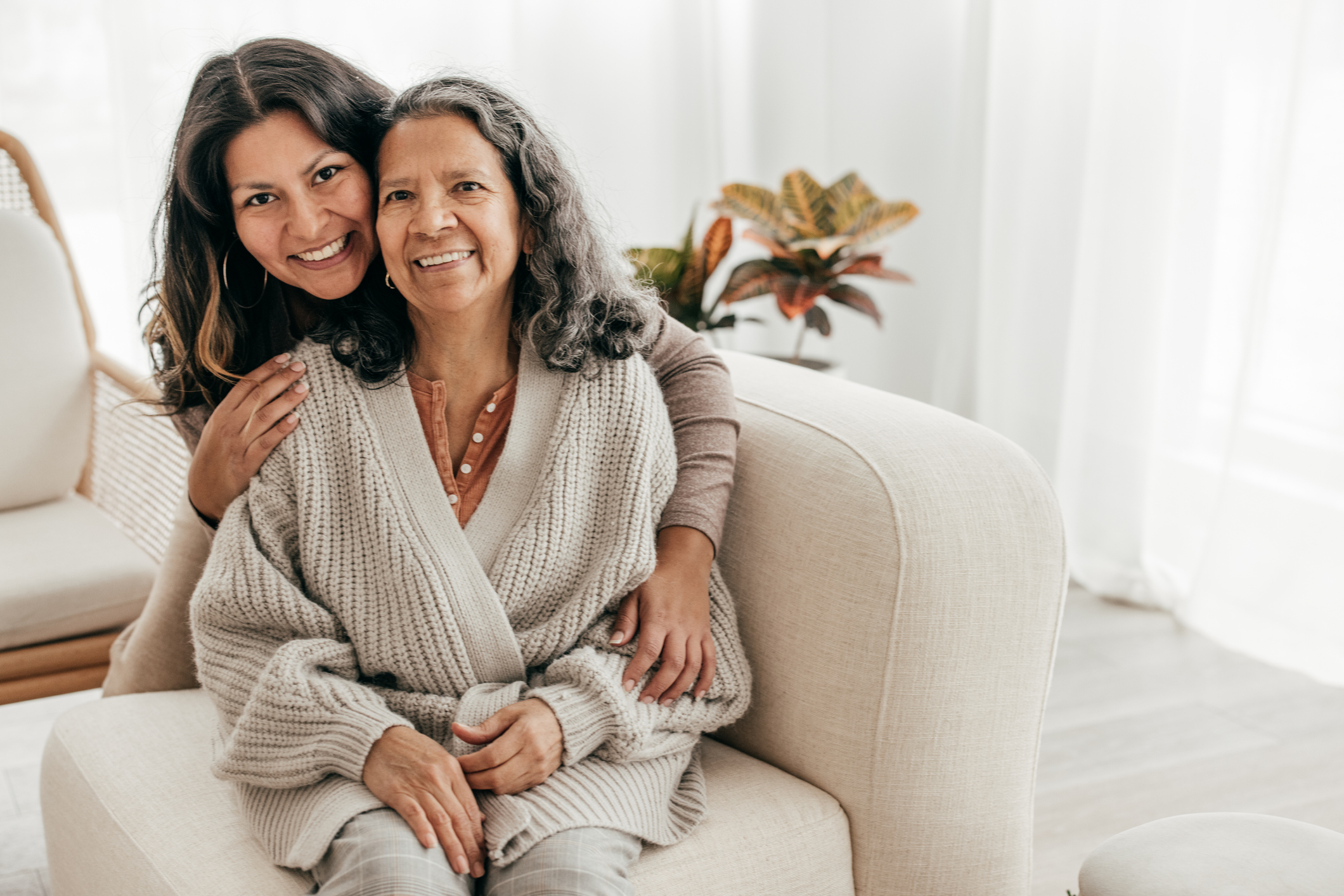 Two people sitting on a couch hugging and looking at the camera.