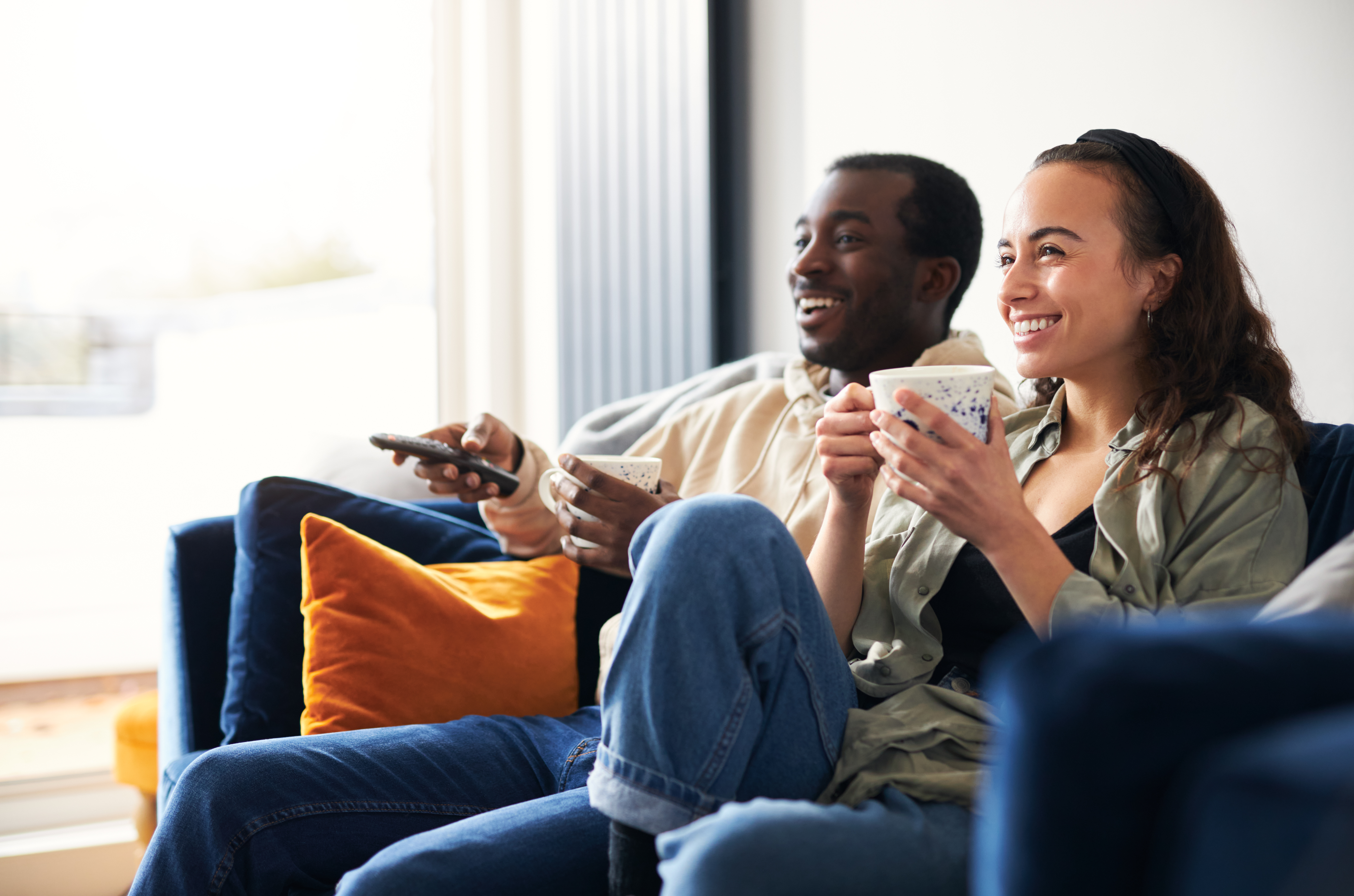 Two people channel surfing from the couch.