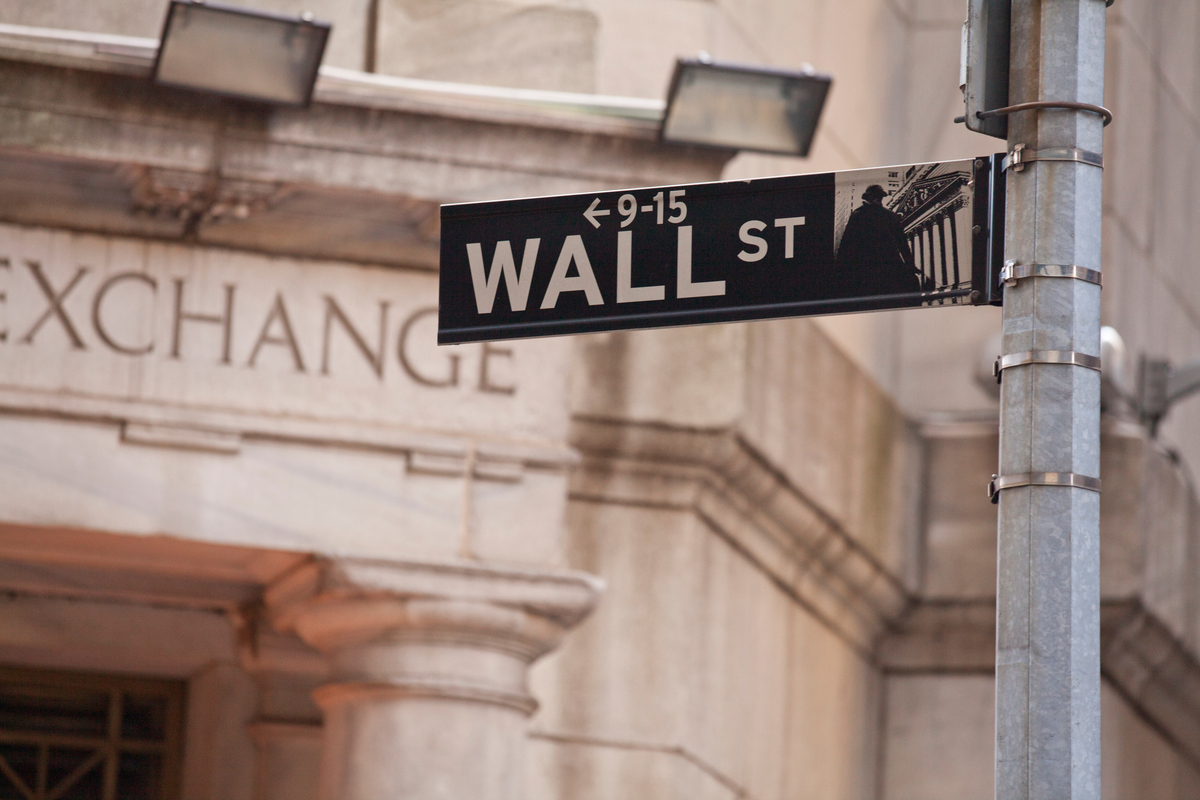 A street sign for Wall St in front of a stone building with the word Exchange above the door.