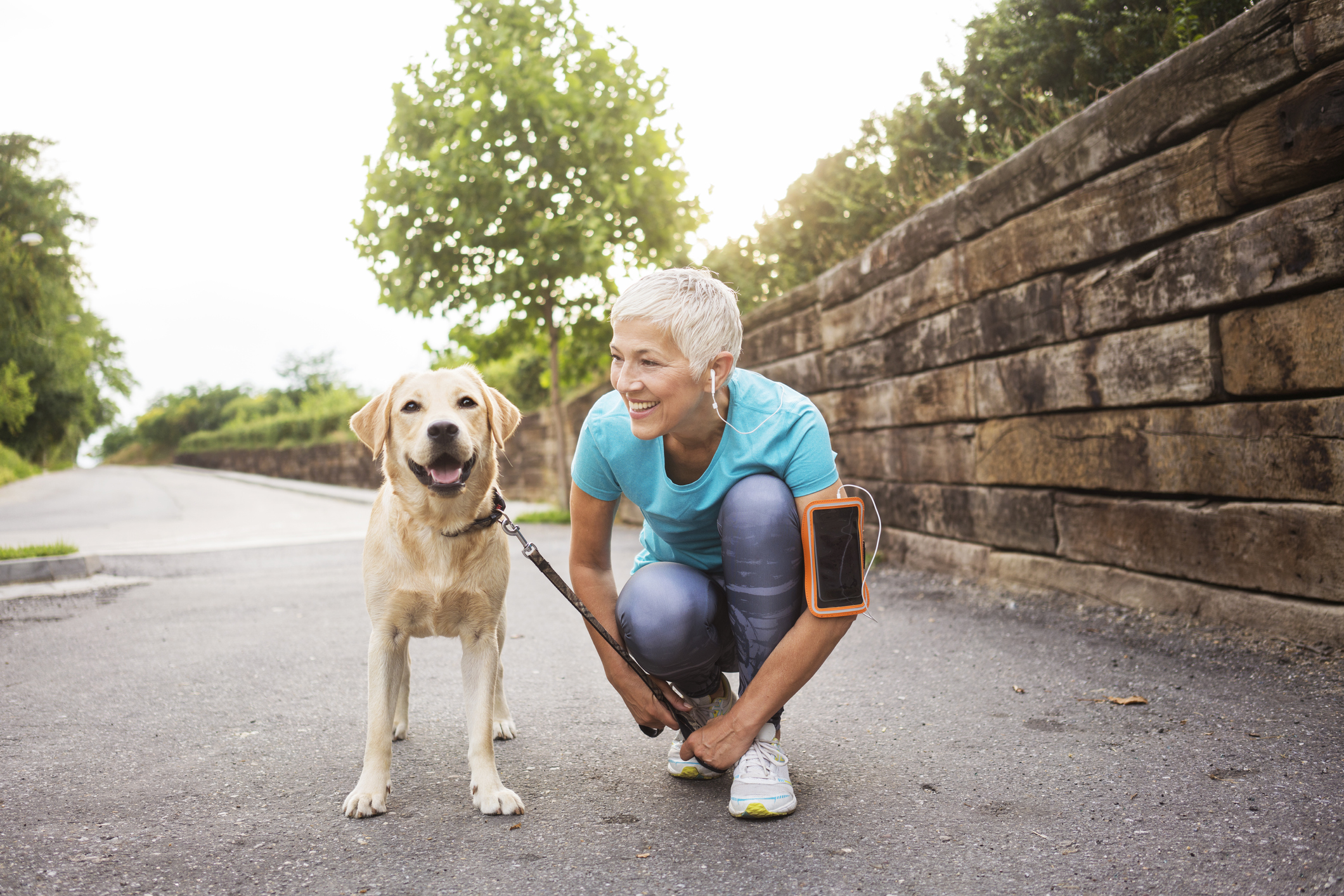 Person outdoors, tying shoe while holding dog on leash.