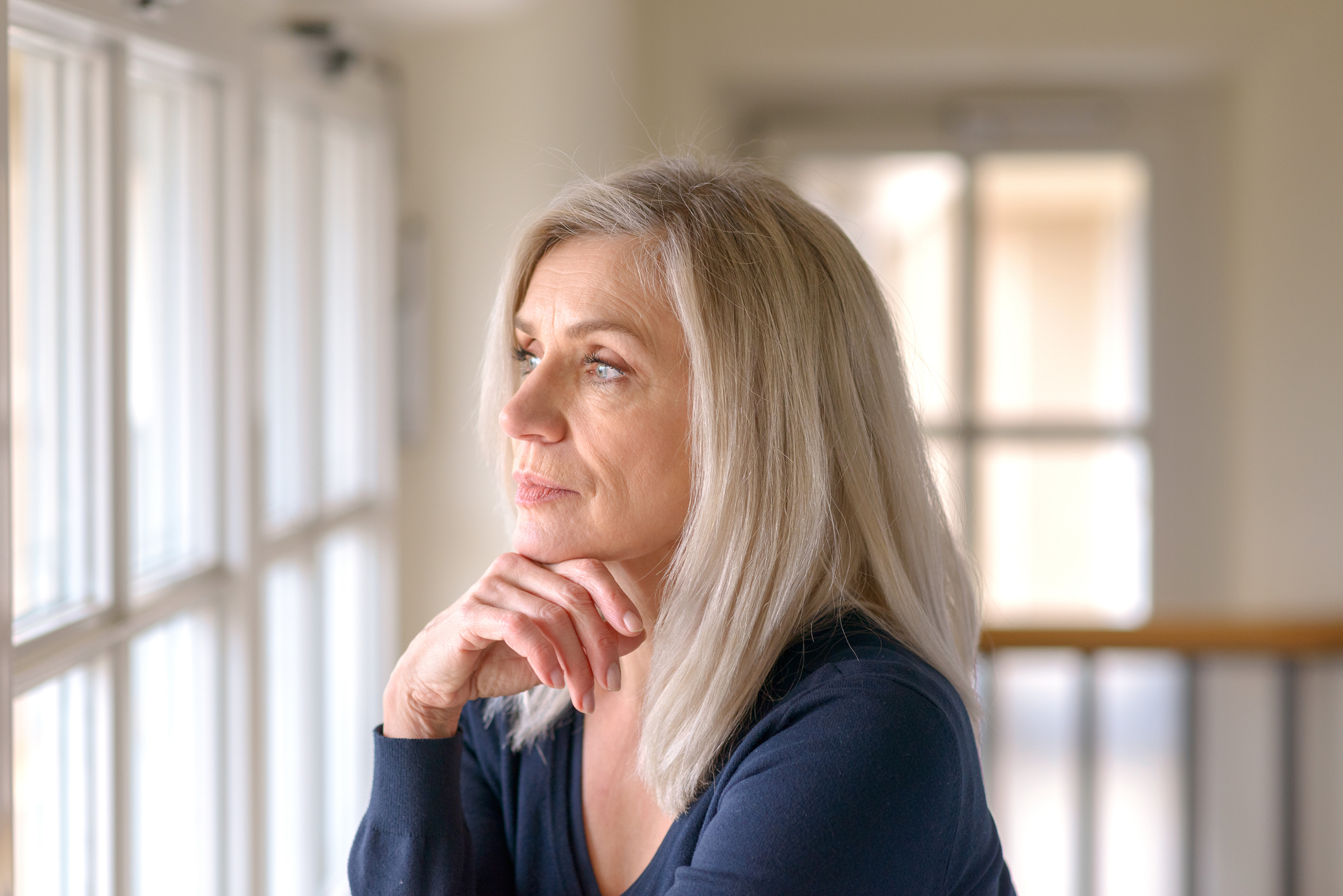 Person with a serious expression looking out a window.