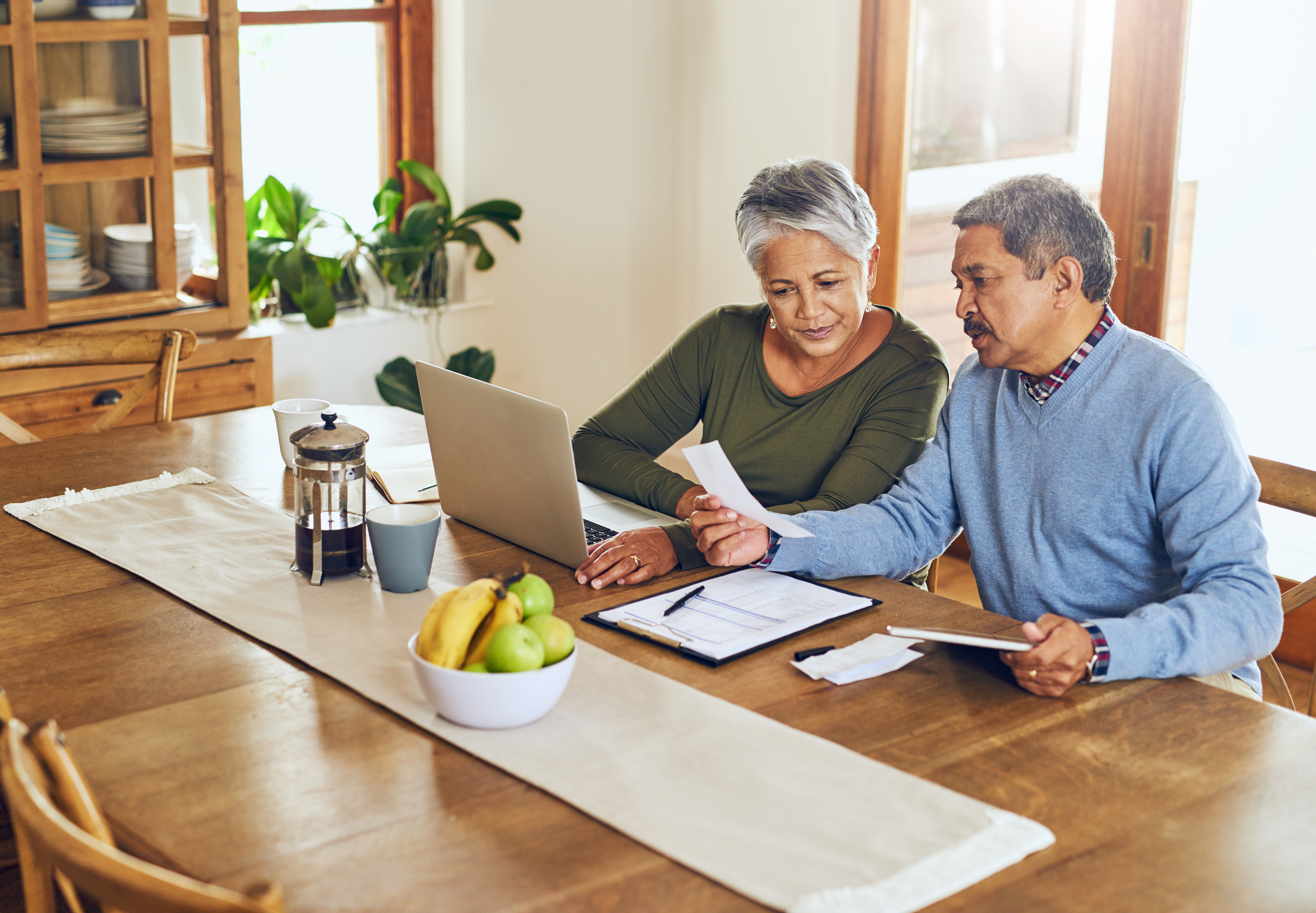 Two people sitting at table with computer and note pad.