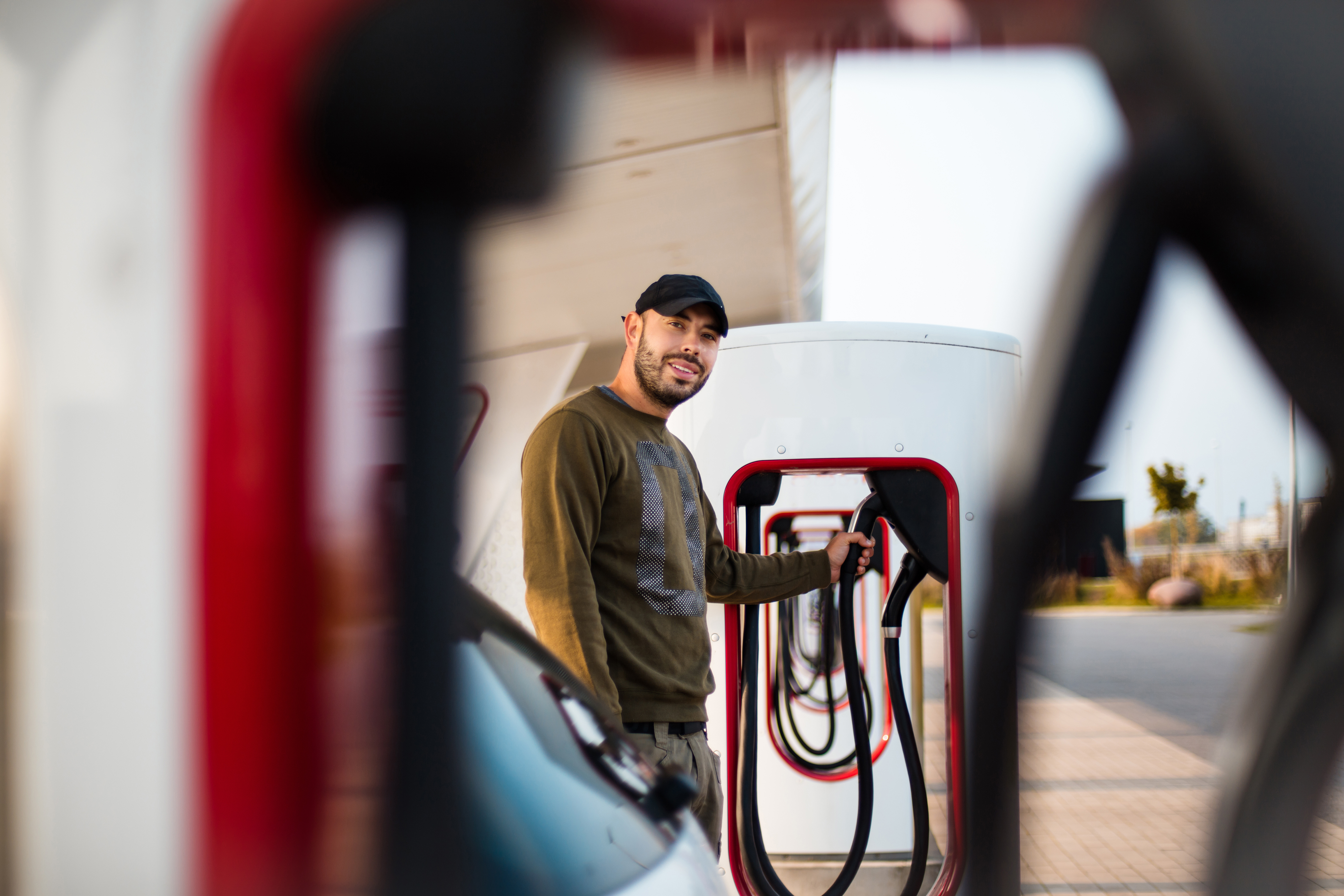 Someone at a Tesla Supercharger station with a hand on the charger.