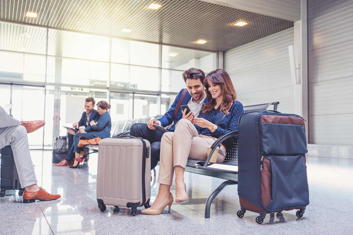 People in business attire seated next to travel luggage at the airport.