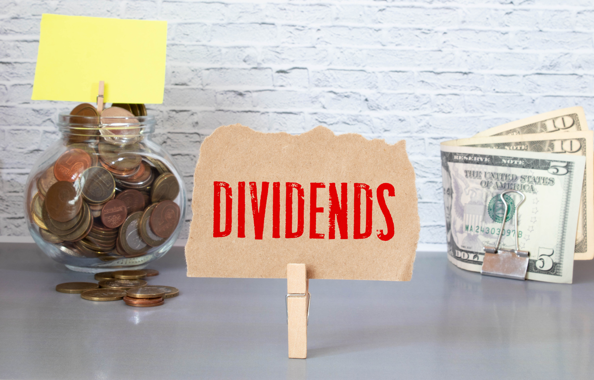 The word dividends held up between a jar of coins and paper money.