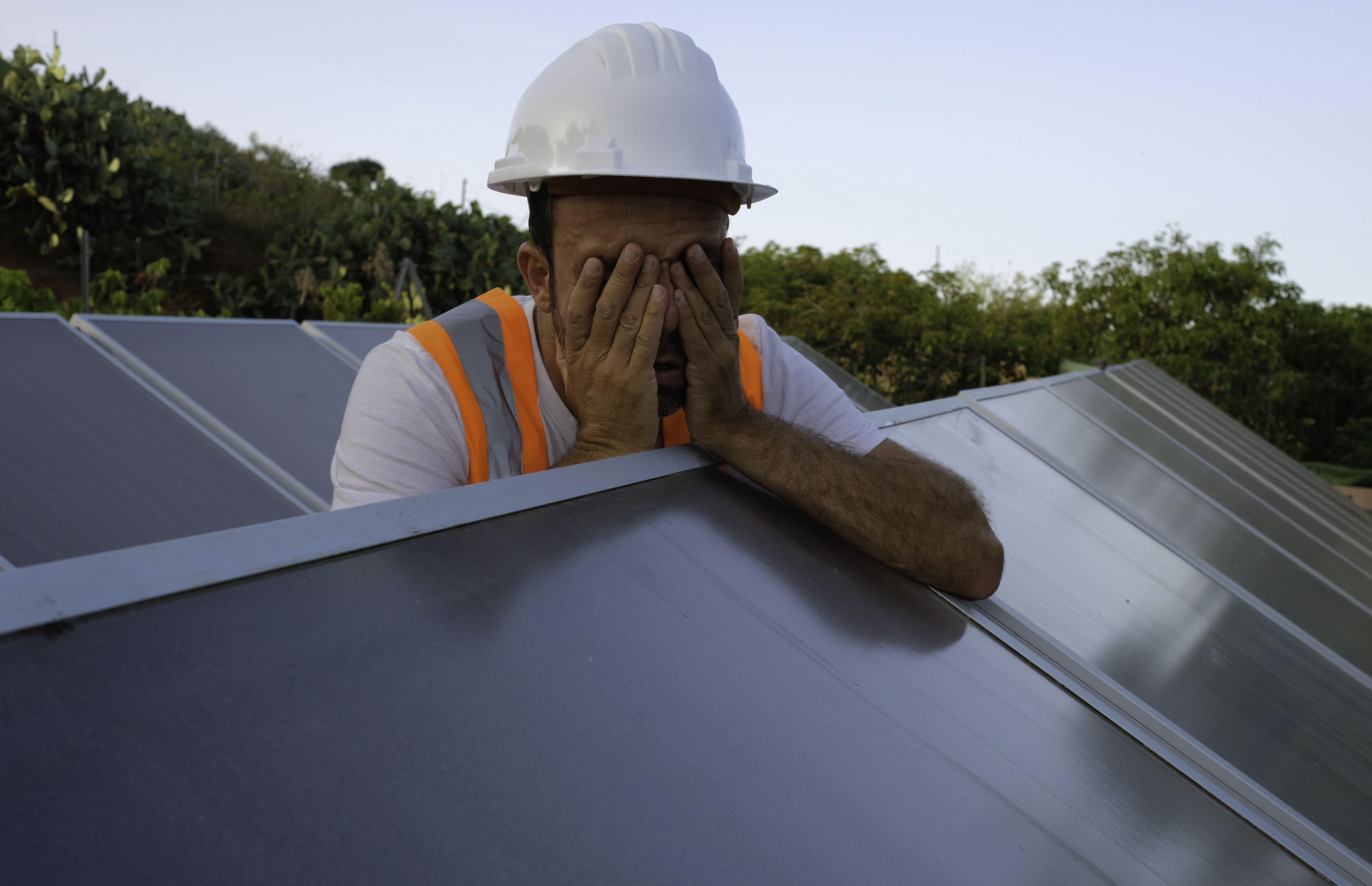 A solar installer covers his face. 