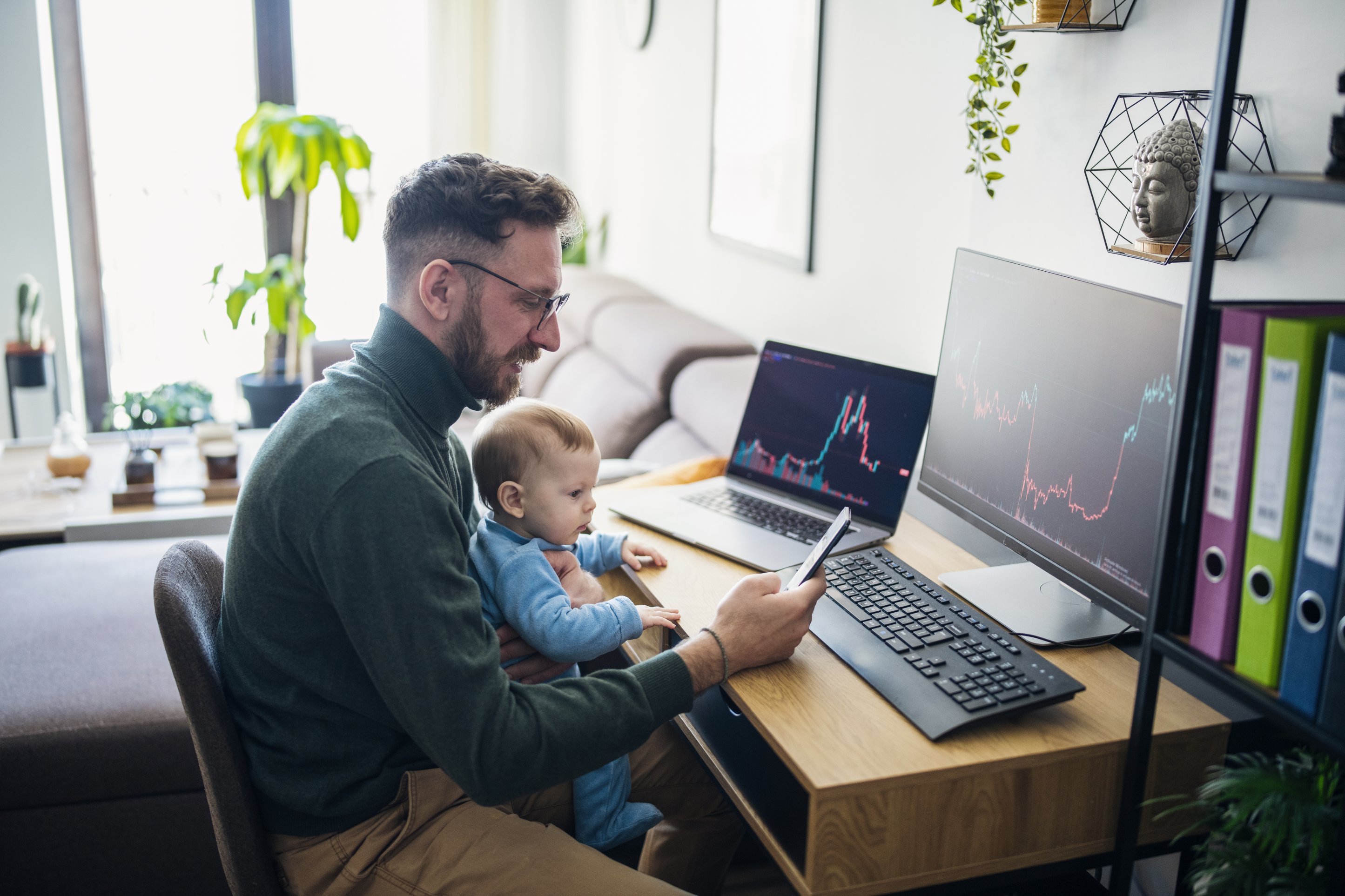 A parent holds a baby while trading stocks.