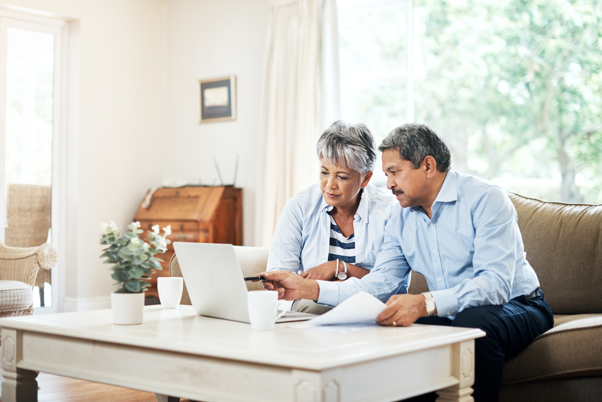 Two people sitting on a couch working with a laptop computer and pieces of paper on a coffee table. 