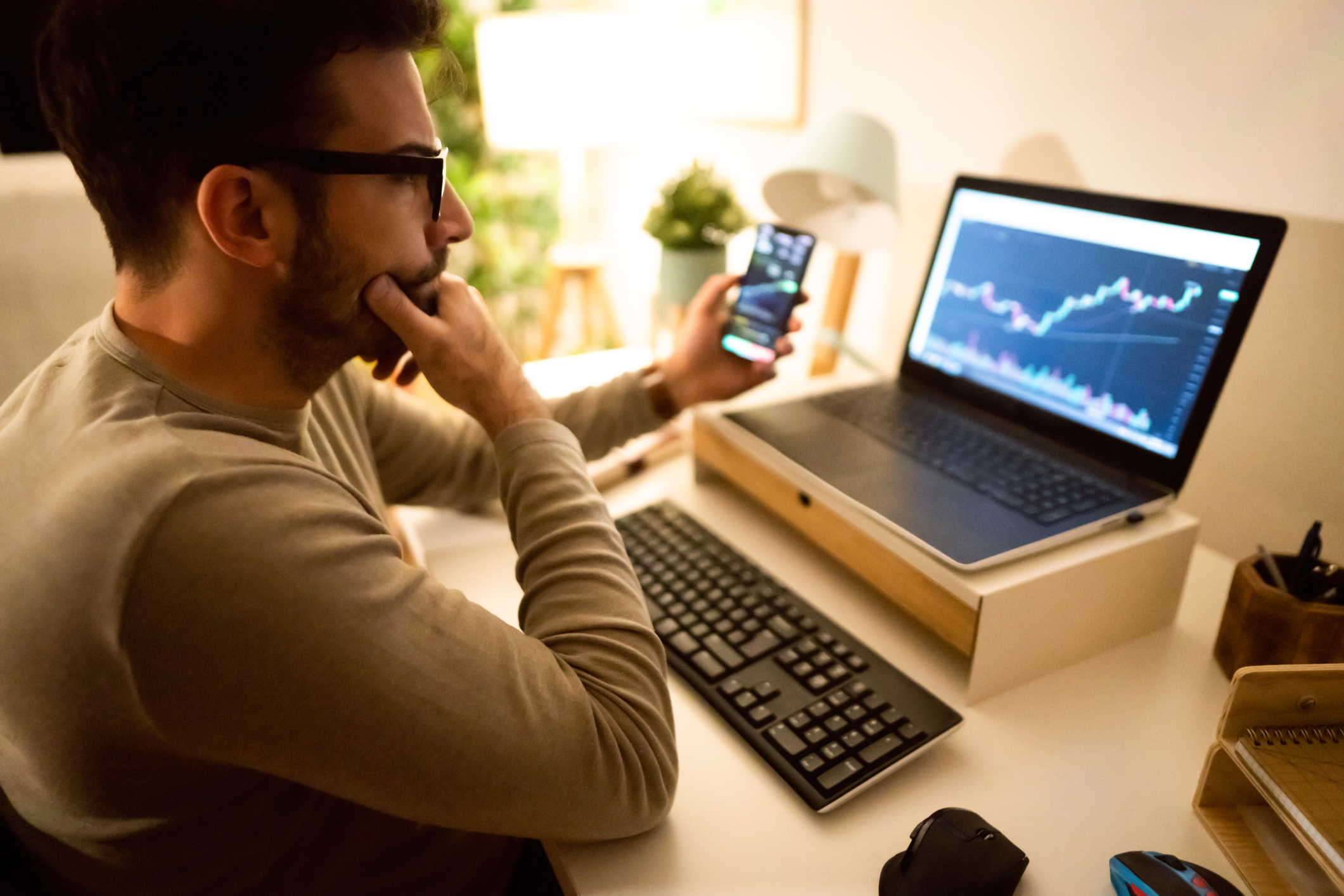 person looking at stock chart on phone and laptop.