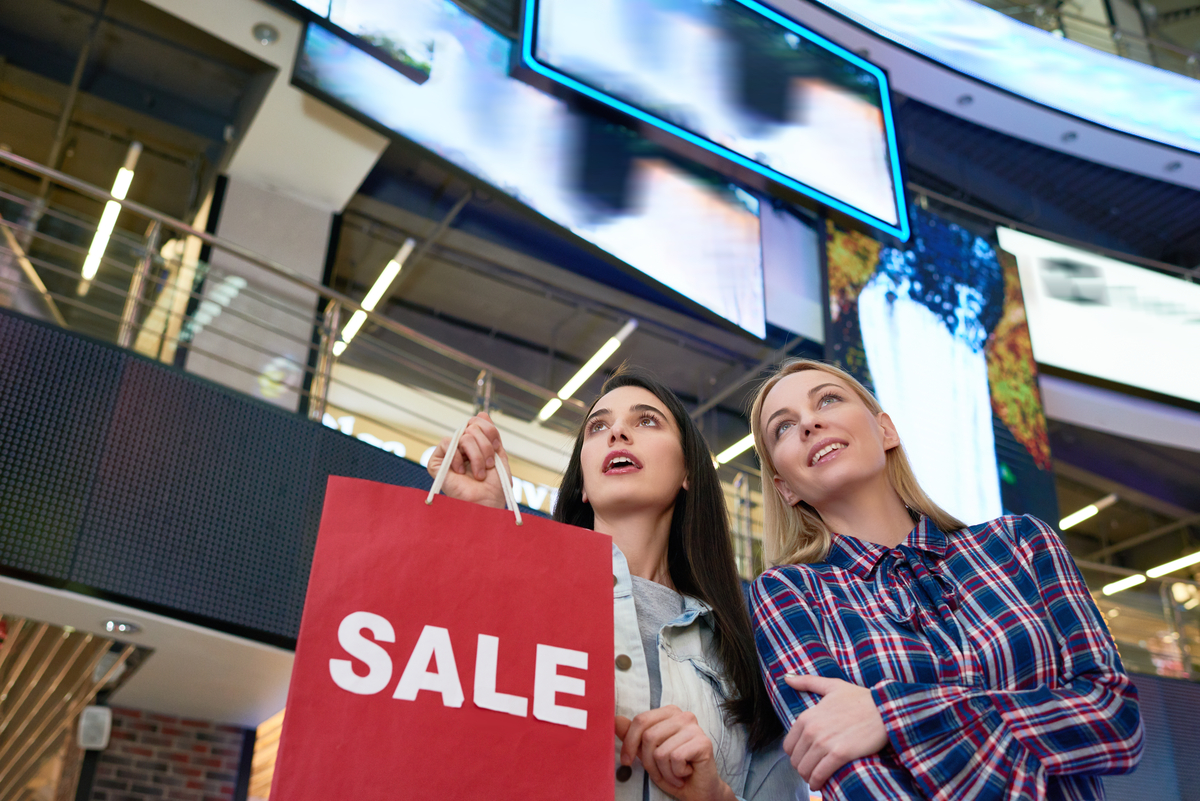 Person holding a shopping bag with SALE spelled out next to a companion in an abstract retail setting.